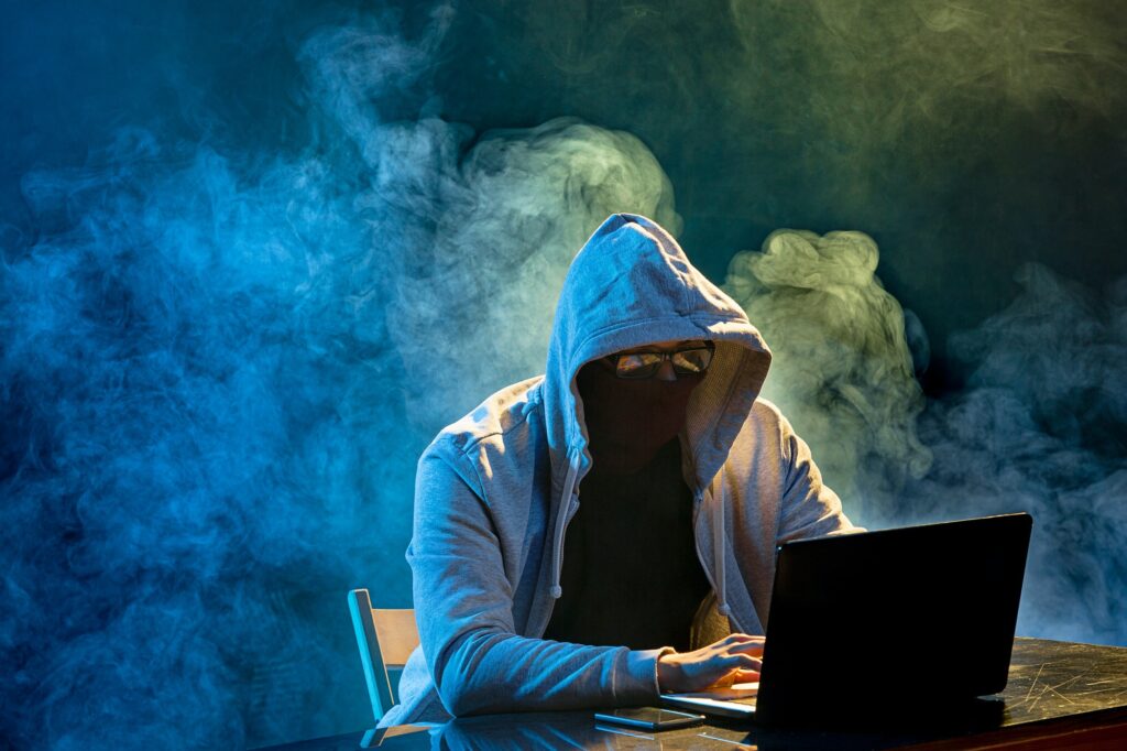 Hooded computer hacker stealing information with laptop